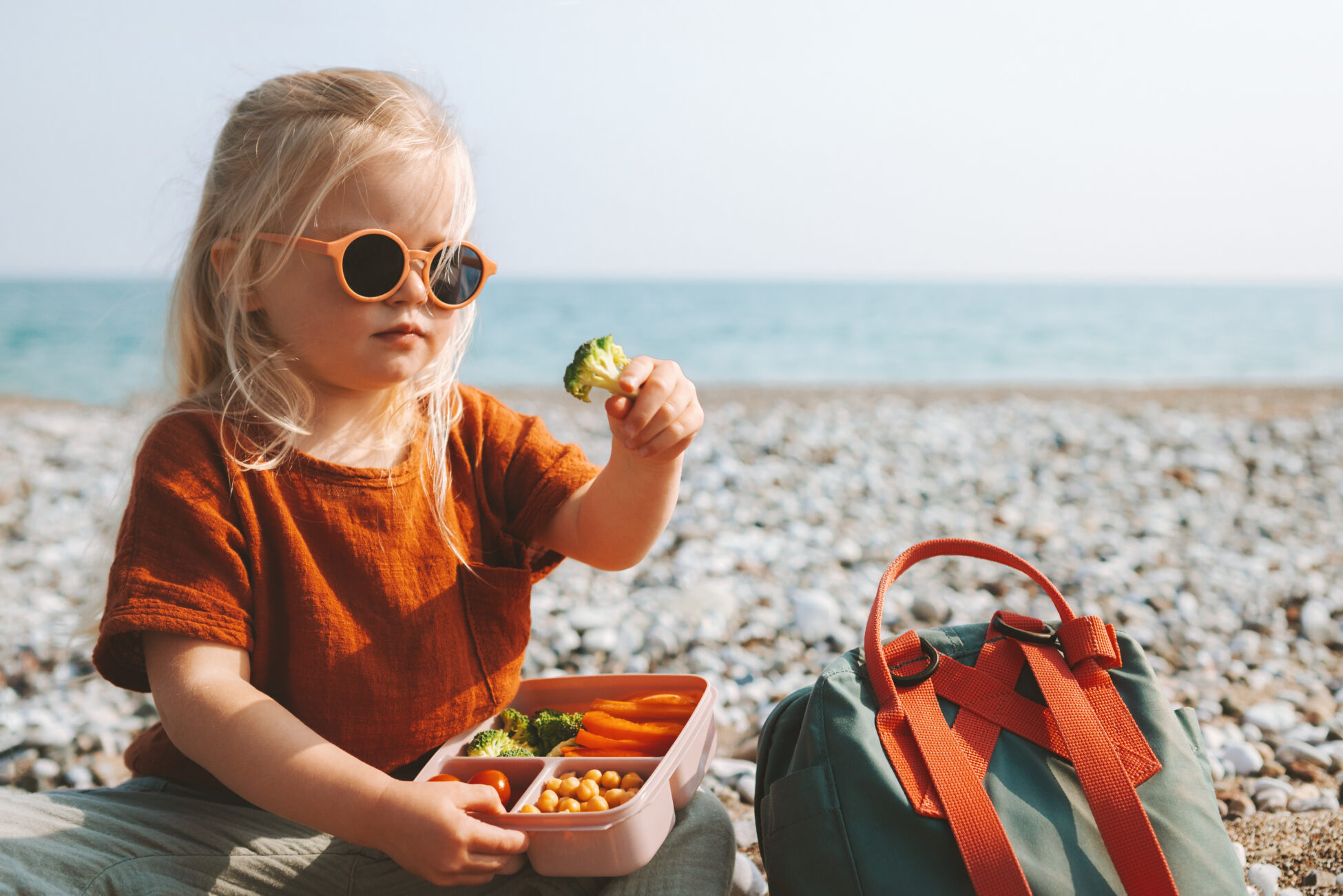 Young girl on beach enjouýing healthy vegetables from lunchbox at the beach